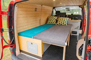 modulé aménagé en bois dans un van rouge avec le lit déplié