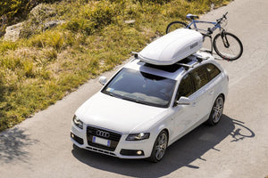 Audi blanche avec un coffre de toit blanc et un vélo derrière