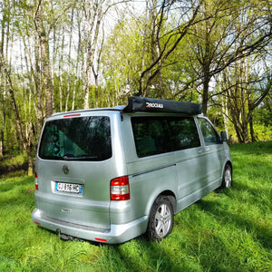 Volkswagen Transporter gris garé dans l'herbe avec un auvent fermé et rangé